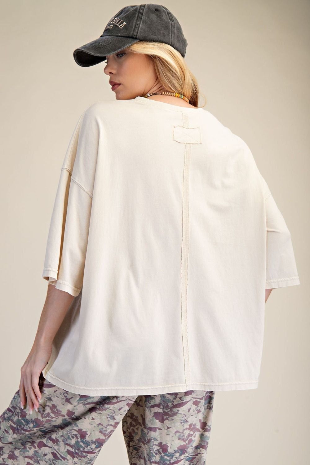 Woman wearing a white shirt and floral pants with a gray cap on a beige background