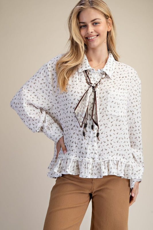 Woman wearing a white floral blouse with a tie and brown pants on a beige background