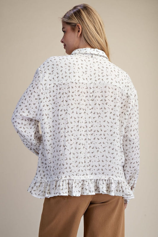 Woman wearing a white floral blouse with long sleeves and brown pants on a beige background