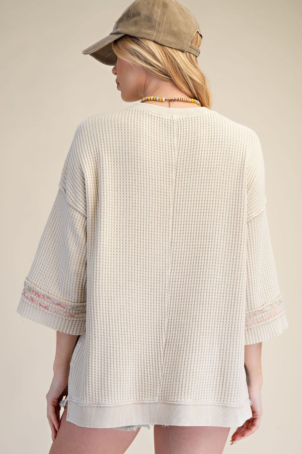 Person wearing a beige textured shirt and cap on a plain background