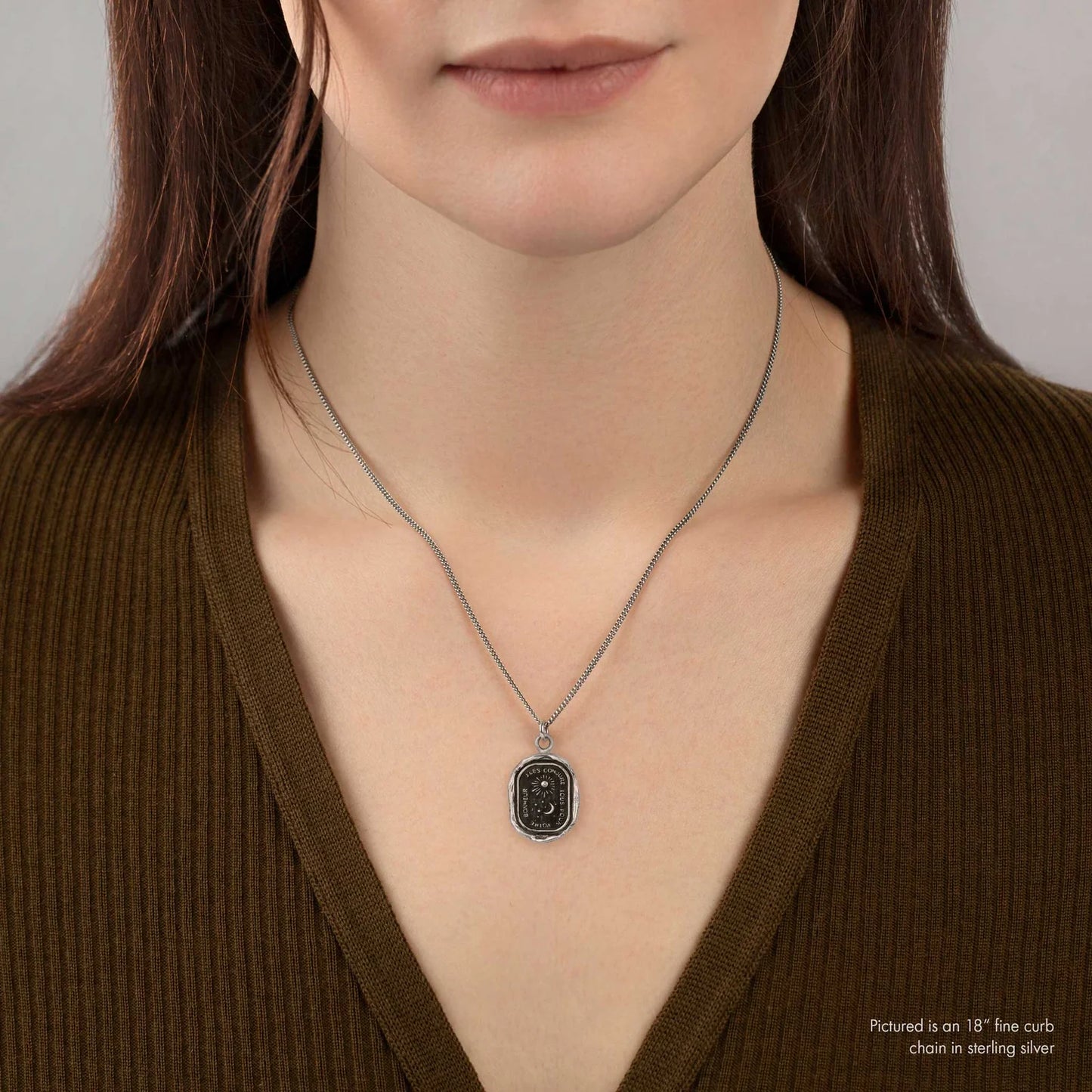 Person wearing a necklace with a pendant on a plain background