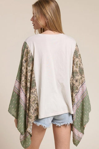 Woman wearing a green patterned scarf over a white top and denim shorts on a beige background