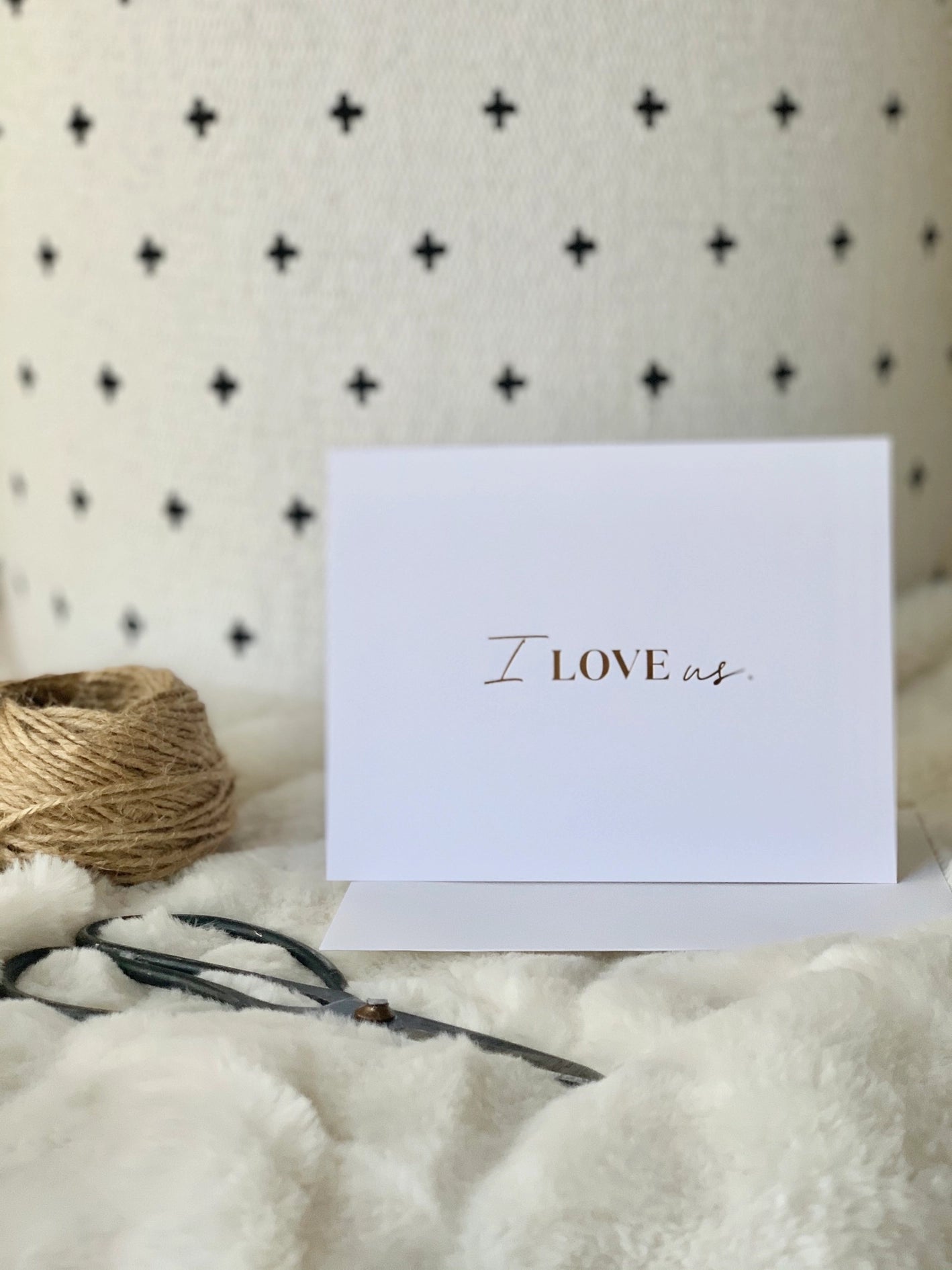 White card with 'I LOVE us' text on a textured surface with twine and ribbon.