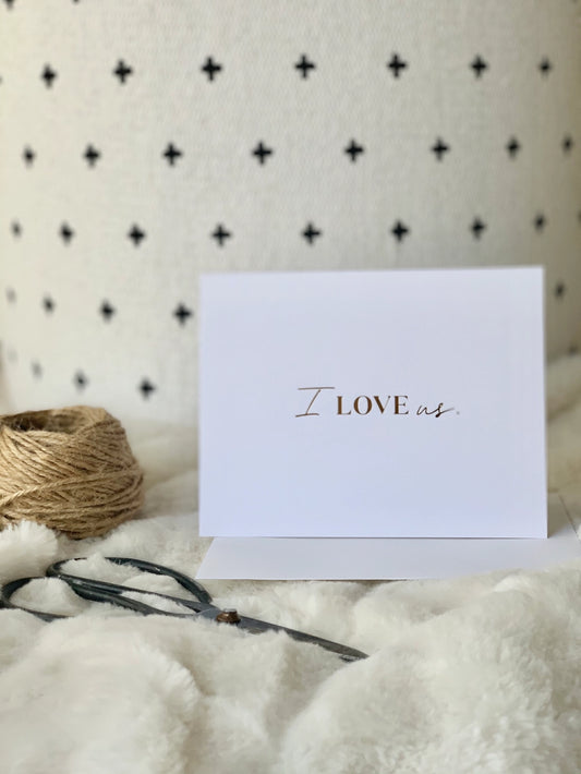 White card with 'I LOVE us' text on a textured surface with twine and ribbon.