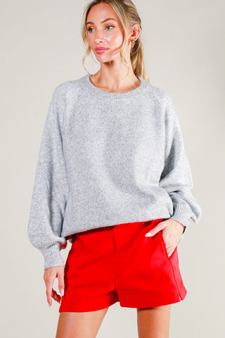 Woman wearing a gray sweater and red shorts against a plain background