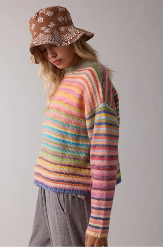 A women wearing a rainbow sweater against a neutral background.