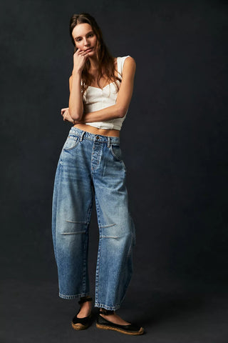 A female model wearing mid-rise, wide-leg barrel jeans with subtle distressed details.