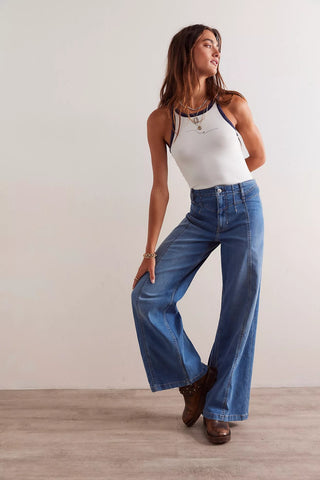 Woman wearing a white tank top and blue jeans against a plain background