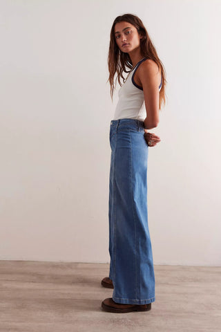 Woman wearing a white tank top and blue jeans standing against a plain background
