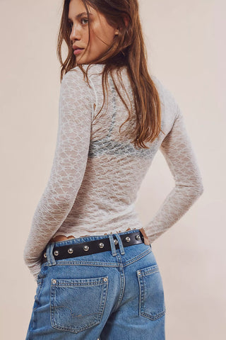 Woman wearing a sheer long-sleeve top and blue jeans against a plain background