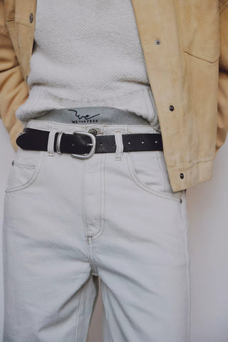 Person wearing a beige jacket, gray sweater, light gray jeans, and black belt.