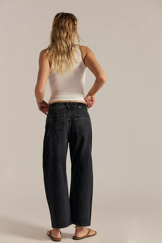Woman wearing a white tank top and dark jeans against a plain background