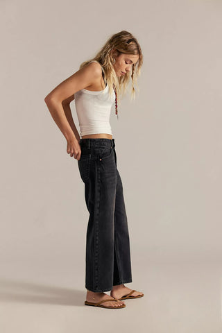 Woman wearing a white tank top and black wide-leg jeans on a beige background
