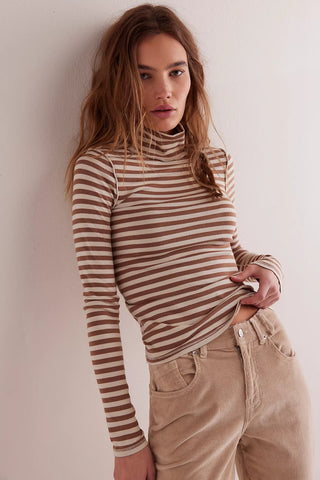 Woman wearing a striped long-sleeve top and beige pants against a plain background