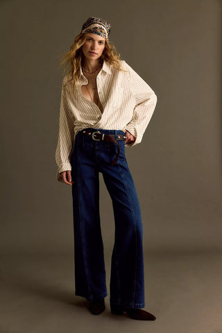 Woman wearing a white blouse, blue jeans, and a patterned headband against a plain background