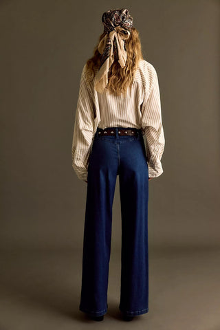 Person wearing a striped shirt and blue jeans with a patterned headscarf on a plain background