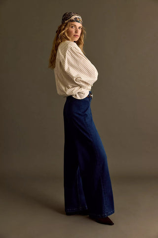 Woman wearing a cream sweater and blue pants against a brown background
