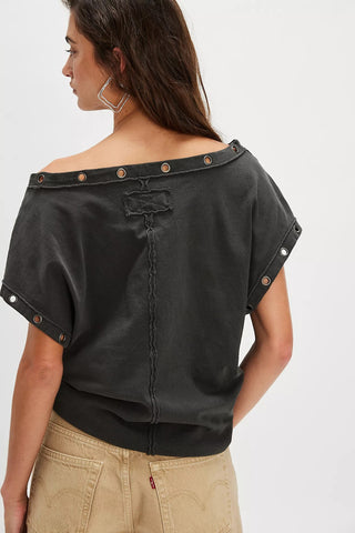 Black off-shoulder top with button details worn by a person on a white background
