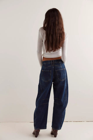 Person wearing dark blue jeans and a white long-sleeve top on a plain background