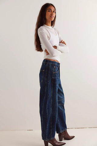 Woman wearing a white long-sleeve top and blue jeans against a white background
