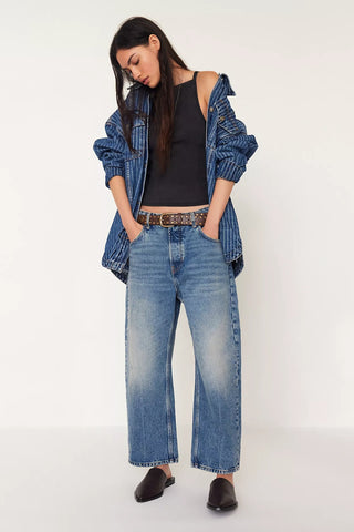 Woman wearing a denim jacket, black top, and wide-leg jeans on a white background