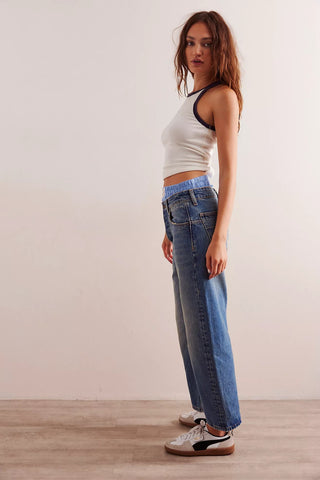 Woman wearing a white tank top and blue jeans standing against a plain background
