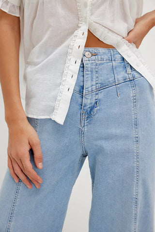 Person wearing light blue jeans and a white blouse with ruffled details.