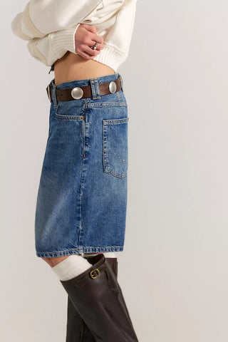 Person wearing a blue denim skirt with a white sweater and brown knee-high boots on a plain background