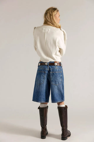 Person wearing a white sweater, blue jeans, and brown boots on a plain background