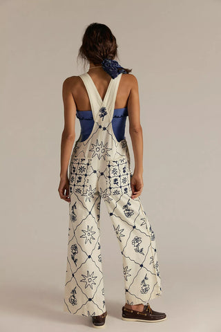 Person wearing a white floral overalls with blue accents on a beige background