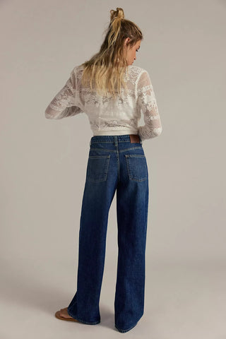 Woman wearing a white lace top and blue jeans on a plain background