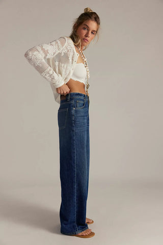 Woman wearing a white lace top and blue jeans against a plain background