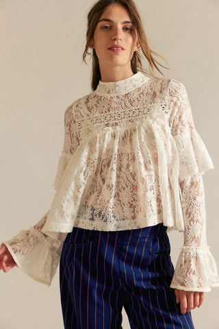 Woman wearing a lace blouse with ruffled sleeves and blue striped pants against a plain background