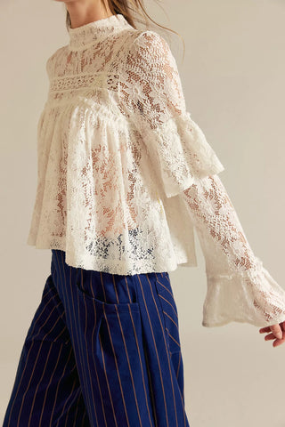 Person wearing a lace blouse with long sleeves and striped pants on a plain background