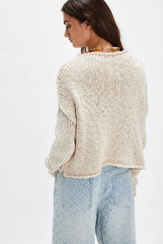 Woman wearing a beige knitted sweater and light blue jeans on a white background