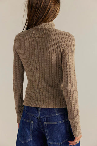 Person wearing a brown cable knit sweater and blue jeans against a plain background