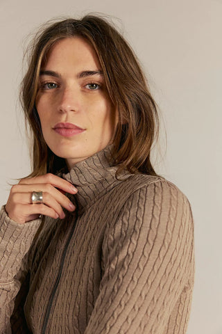 Woman wearing a beige cable knit sweater against a plain background