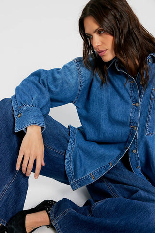Woman wearing a blue denim outfit sitting on a white stool against a white background