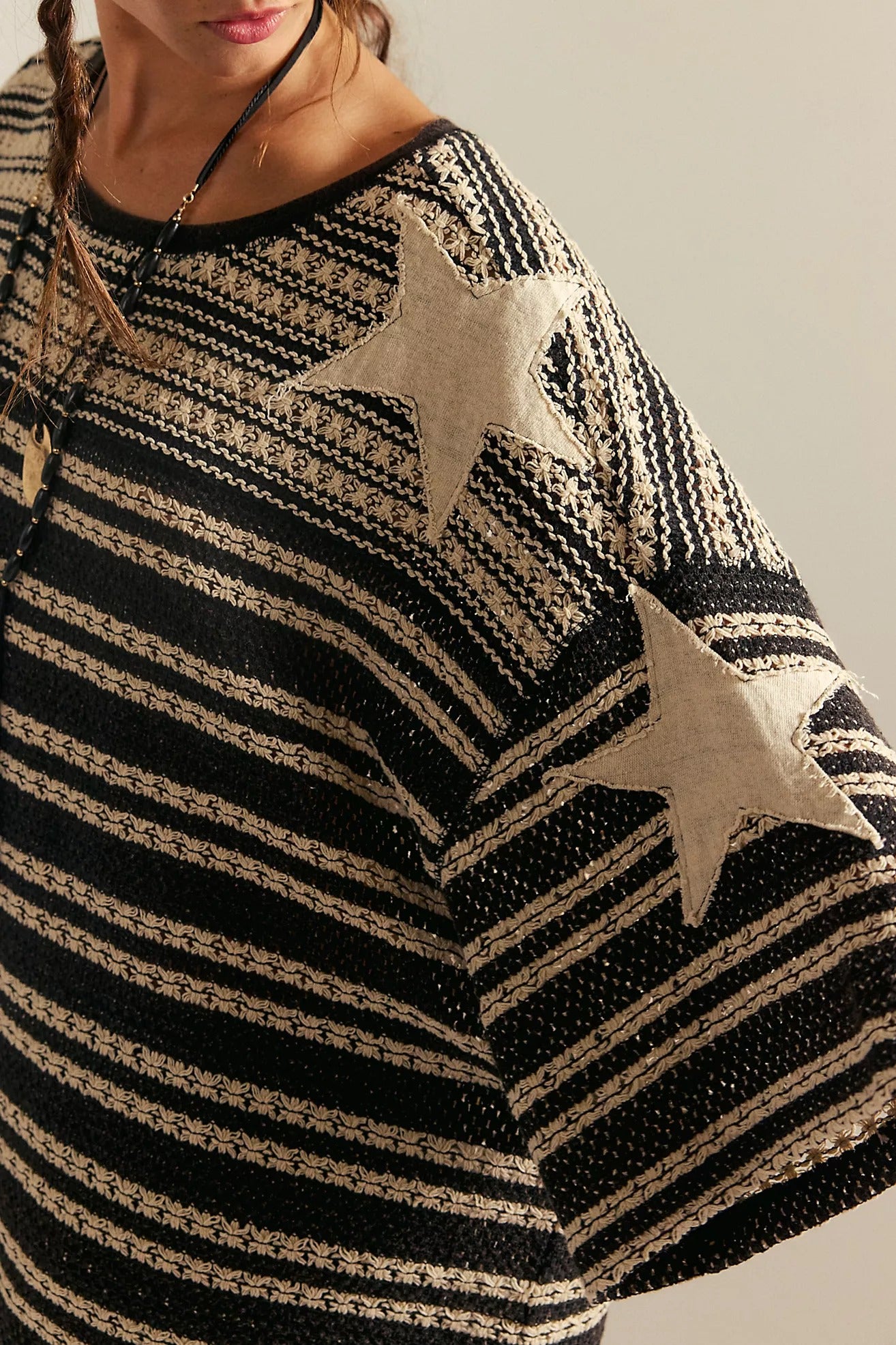 Black and beige striped sweater with star patterns worn by a person.