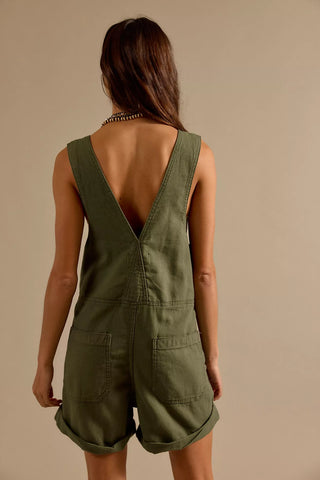 Person wearing green overalls with a beige background