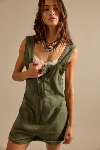 Woman wearing a green overall dress against a beige background