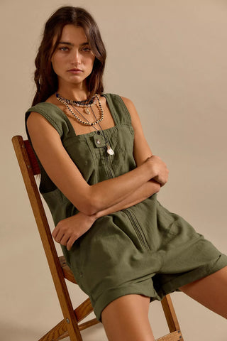 Woman wearing an olive green dress sitting on a wooden chair against a beige background