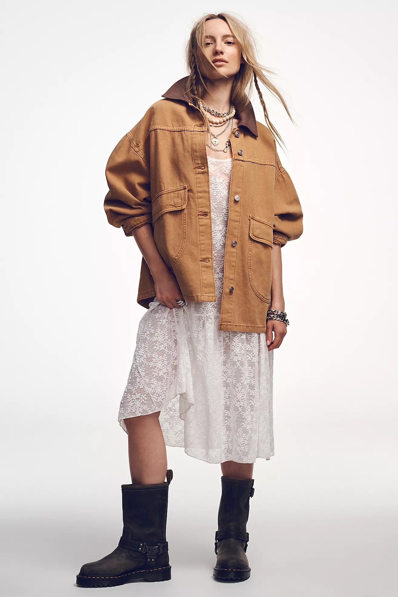 Woman wearing a brown jacket, white dress, and black boots on a white background