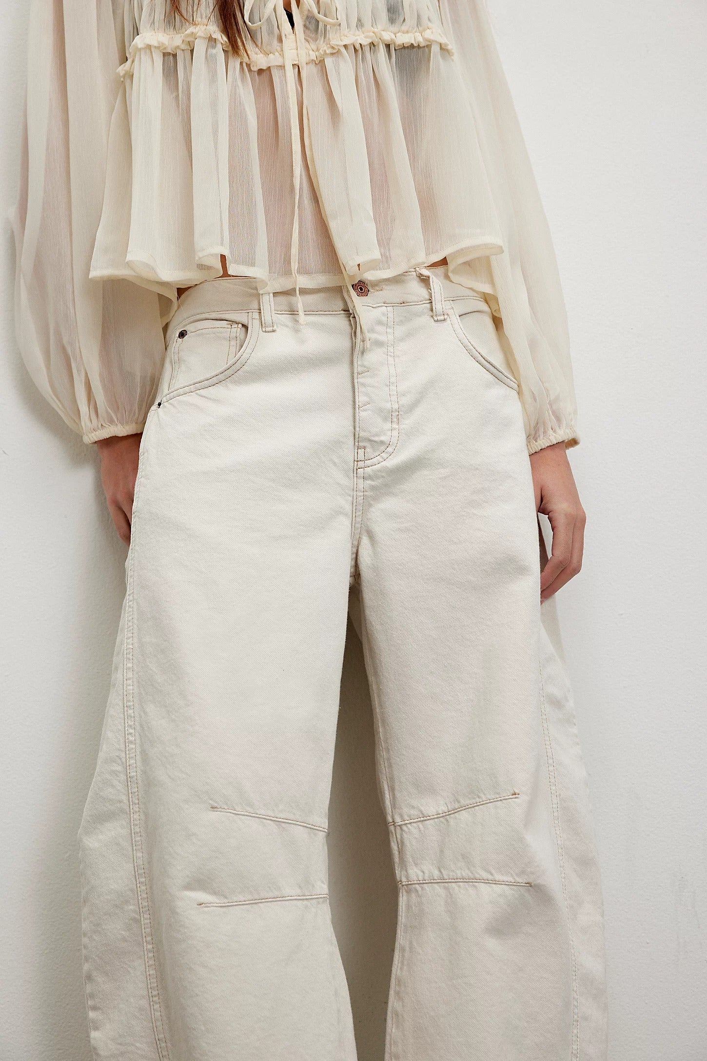 Person wearing a sheer beige blouse and light-colored jeans against a white background