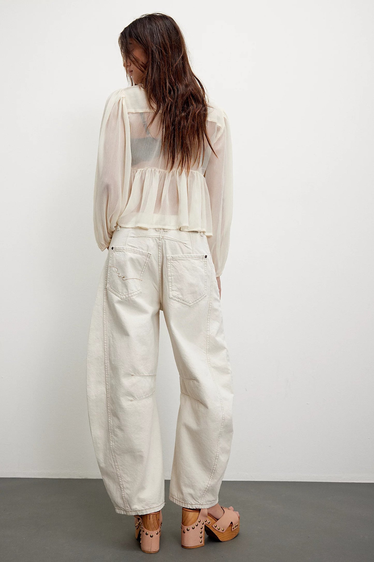 Woman wearing a sheer white top and light-colored pants against a plain background