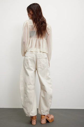 Woman wearing a sheer white top and light-colored pants against a plain background