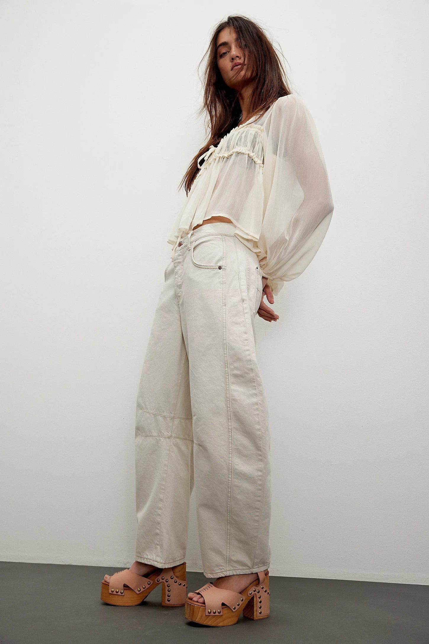 Woman wearing a sheer white top and beige pants against a plain background