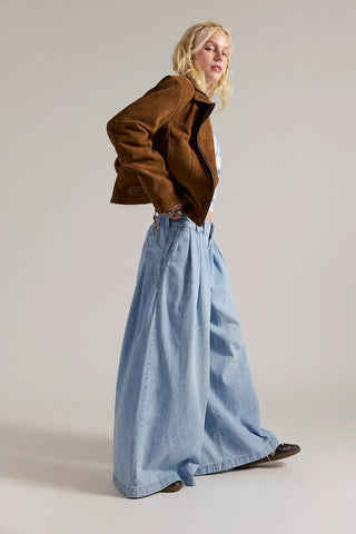 Woman wearing a brown jacket and blue denim pants on a plain background