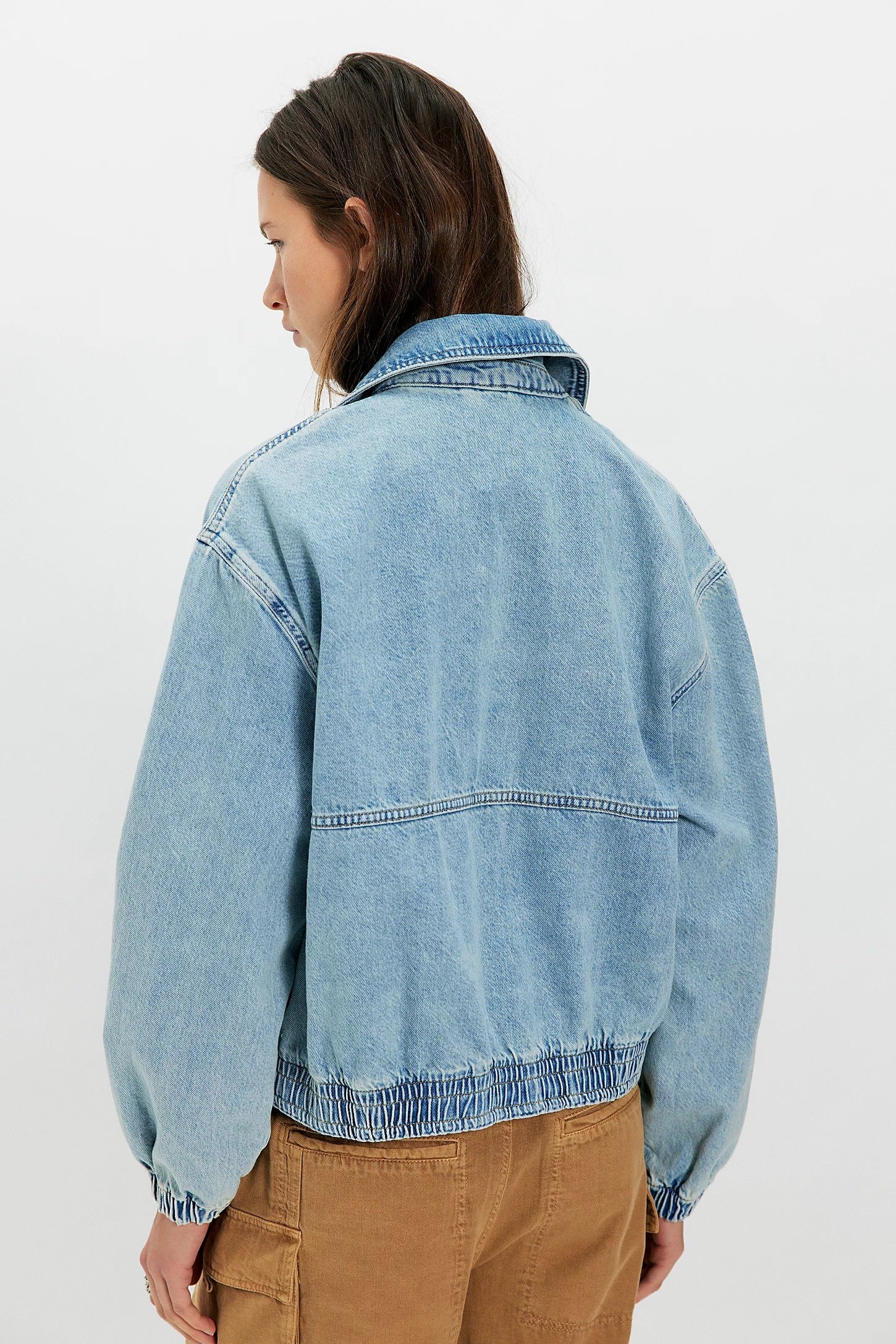 Person wearing a light blue denim jacket on a white background