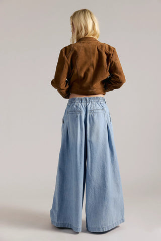 Person wearing a brown jacket and blue wide-leg jeans on a plain background